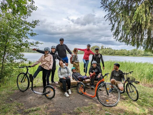 Tõukerattamatk ümber Pühajärve. Grupp matkalisi on kogunenud pildistamisele RMK Kooliranna lõkkekohas, järveäärses ujumiskohas. Lahe ja rõõmus foto. Mida teha suvel Otepääl?