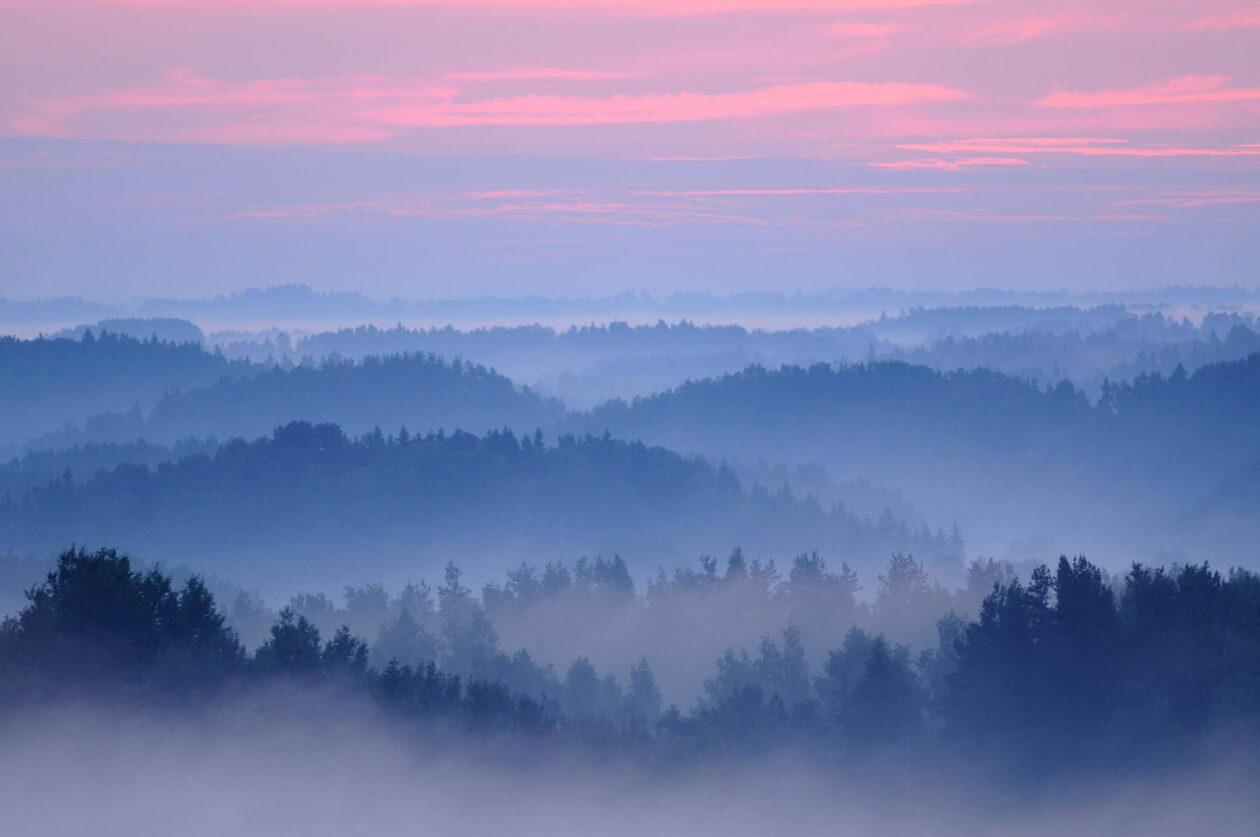 Ilus kõrge maastikuvaade puude latvadest kaugusesse. Sinakas ja oranž loojang. Loodusfotografia. Fotomatkad Lõuna-Eestis.
